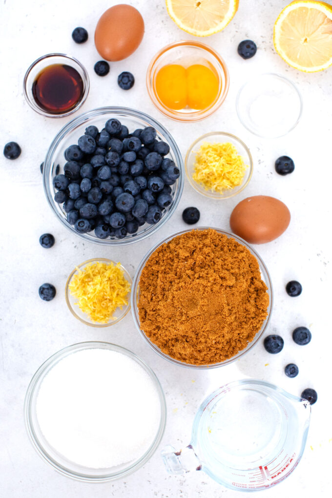 Overhead shot of blueberry french custard cake ingredients in bowls on a white surface.