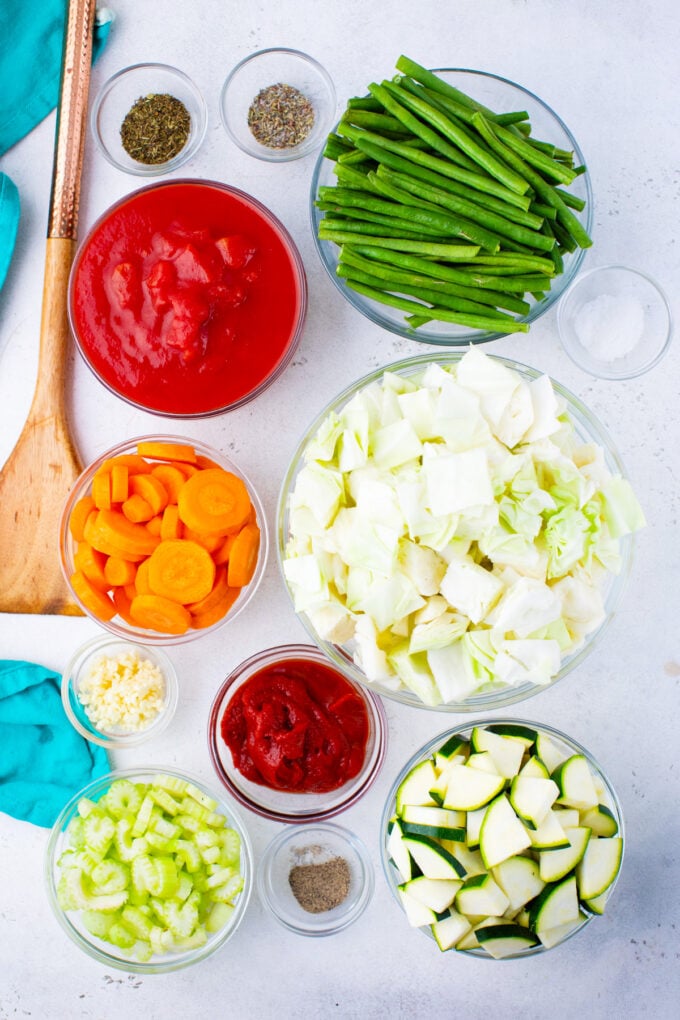 Ingredients for cabbage soup in bowls on a white surface.