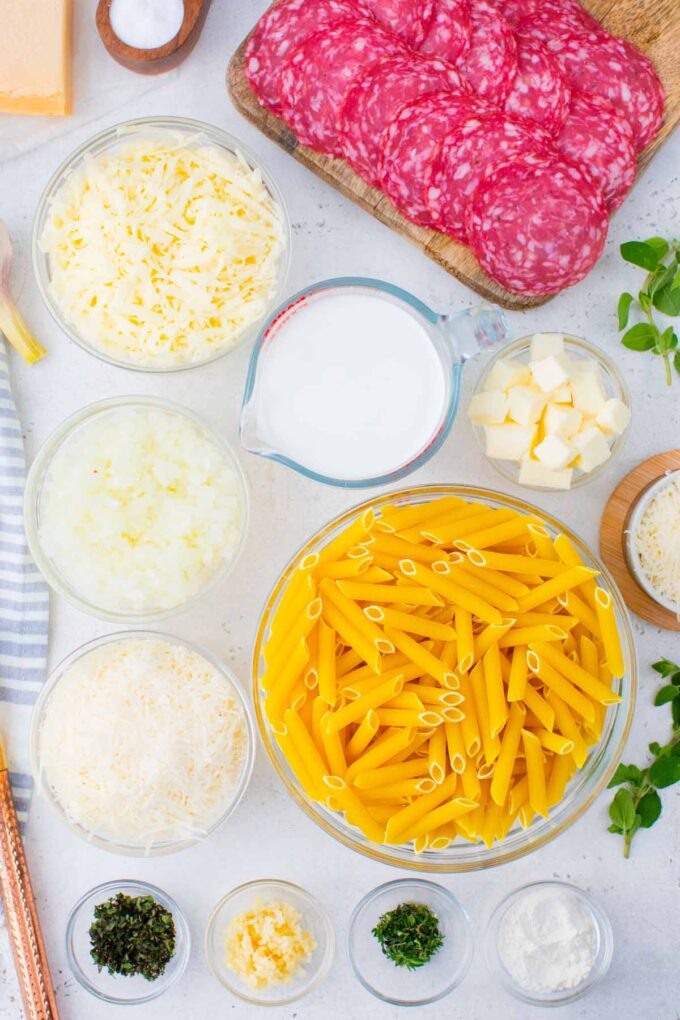Overhead shot of white pizza casserole ingredients in bowls on a white surface.