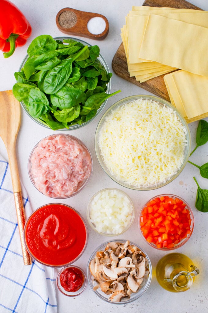 Overhead shot of chicken spinach lasagna ingredients on a white surface.