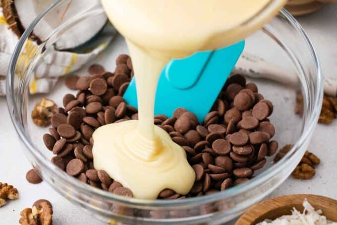 adding condensed milk to a bowl with chocolate chips