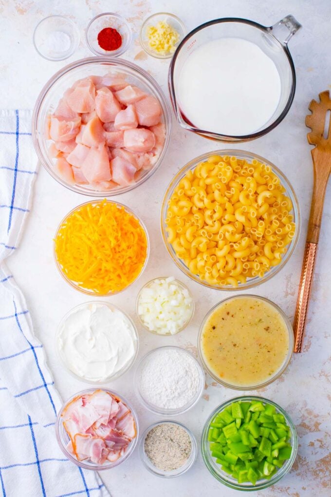 Overhead shot of cheesy crack chicken casserole ingredients in bowls on a white surface.