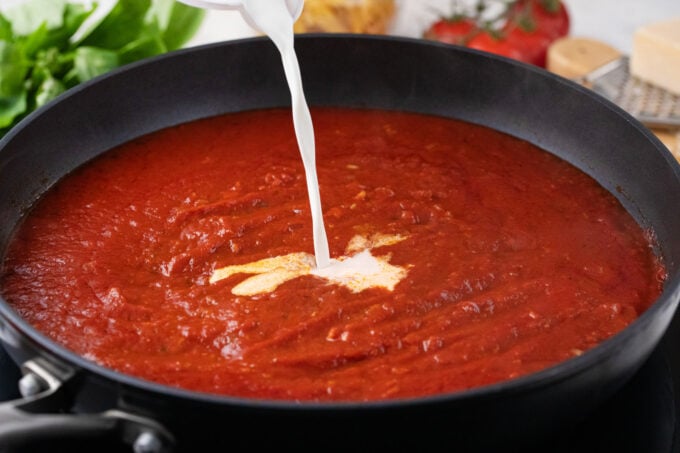 Adding cream to tomato sauce.