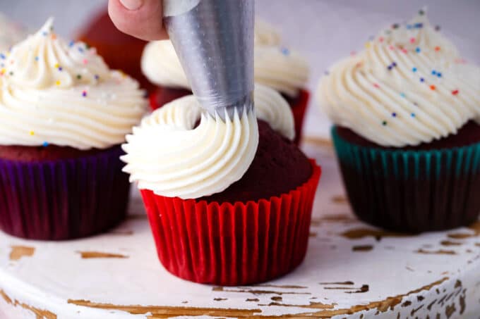 Piping cream cheese frosting onto a red velvet cupcake.