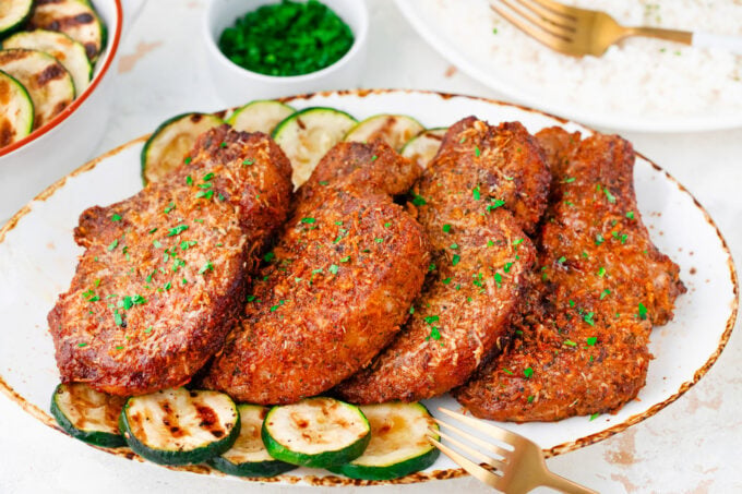 A plate of crispy air fryer pork chops with zucchini rounds.