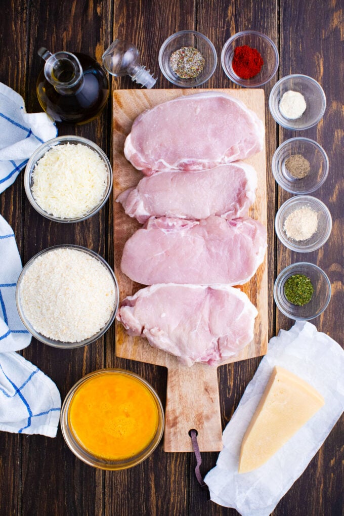 Overhead shot of crispy baked pork chops ingredients in bowls around a cutting board with raw pork chops.