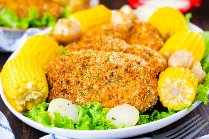 A serving plate with crispy baked pork chops and corn on the cob.