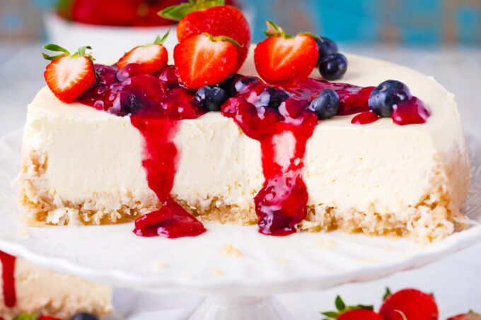 Keto cheesecake sliced in half on a cake stand, with berry sauce dripping off.