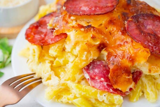 Close shot of a plate of white pizza casserole with pasta and pepperoni.