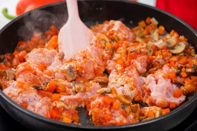 Cooking ground chicken, tomato paste, and veggies in a skillet.