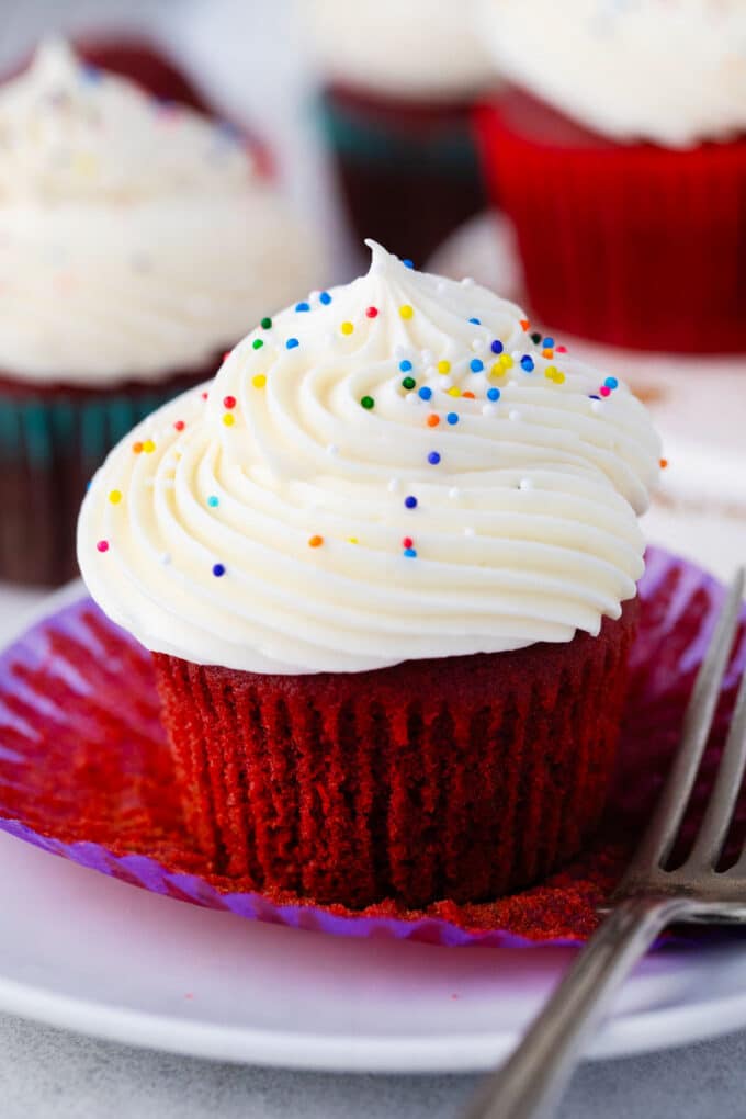 Red velvet cupcake topped with homemade cream cheese frosting and sprinkles.