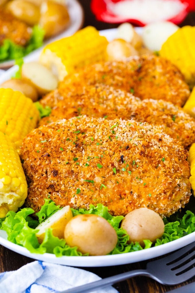 A plate with crispy baked pork chops with potatoes and corn on the cob.