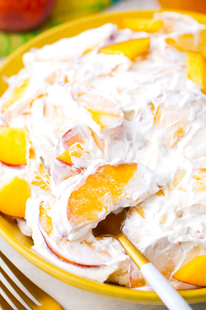 A bowl of creamy peach cheesecake salad with fresh peaches.