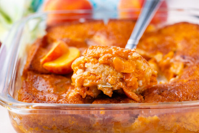 A serving spoon of homemade peach cobbler.