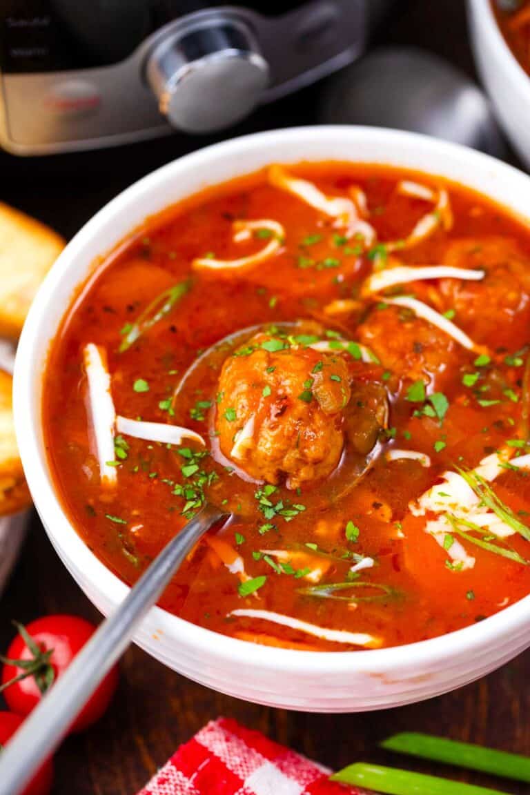A bowl of Instant Pot Italian meatball soup topped with fresh parsley and shredded cheese.
