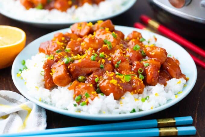 a plate of rice topped with instant pot orange chicken recipe with chopsticks and an instant pot next to it