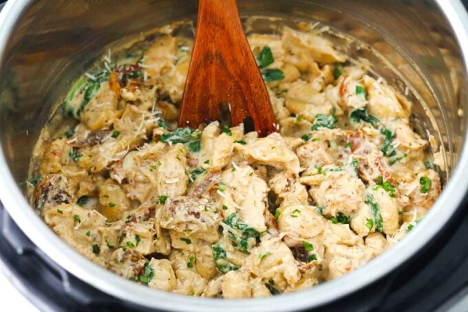 instant pot tuscan chicken pasta with a wooden spoon in it