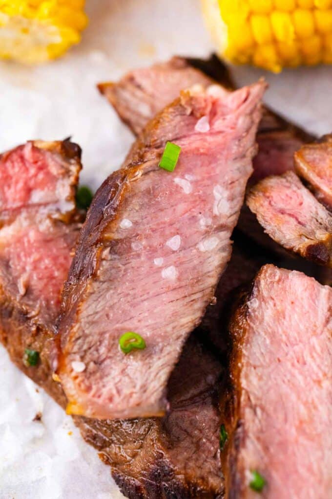 Close shot of slices of juicy Asian style grilled rib-eye steak topped with sea salt and chopped green onions.
