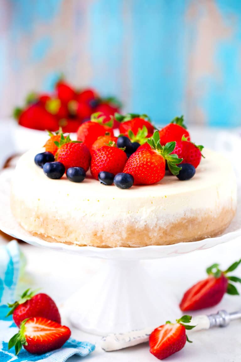 Keto cheesecake topped with berries on a cake stand.