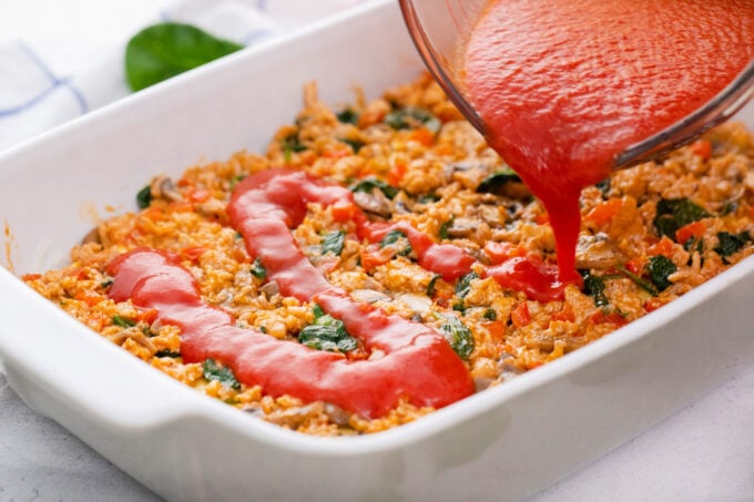 Adding marinara sauce to chicken spinach lasagna.