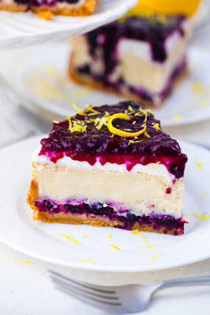 A slice of blueberry french custard cake with lemon frosting, blueberry sauce and lemon zest.