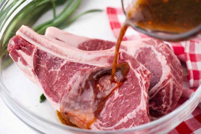 Pouring Asian style steak marinade over two ribeye steaks in a bowl.