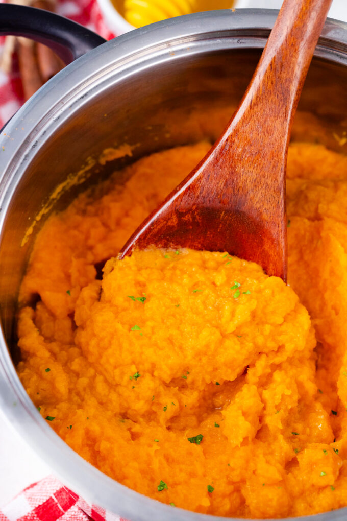 A wooden spoon with creamy and fluffy mashed sweet potatoes.