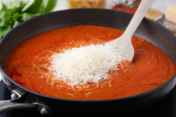 Adding parmesan cheese to penne alla vodka.