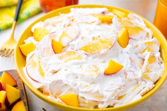 A bowl of creamy peach cheesecake salad with sliced peaches.
