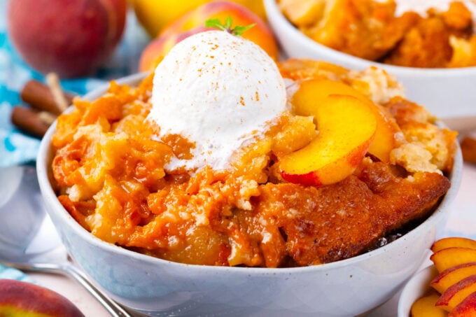 A bowl of homemade peach cobbler topped with ice cream and fresh peaches.