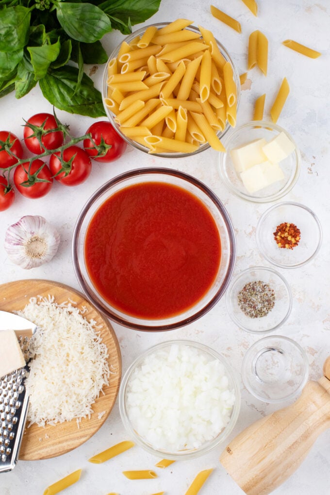Overhead shot of penne alla vodka ingredients in bowls on a white surface.