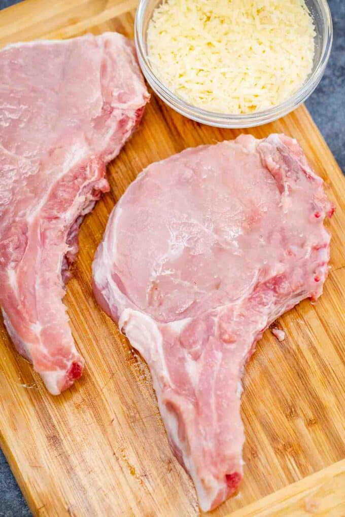 two raw pork chops on a cutting board with a bowl on panko bread crumbs