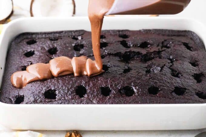 pouring chocolate sauce on top of a poked chocolate cake