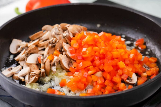 Sautéing mushrooms and bell pepper in a skillet.