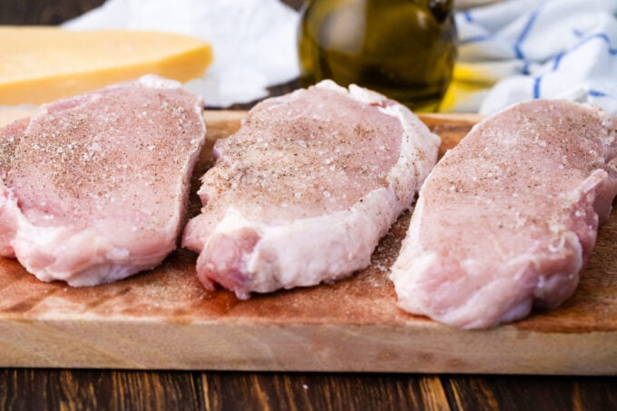 Seasoning raw pork chops on a cutting board.