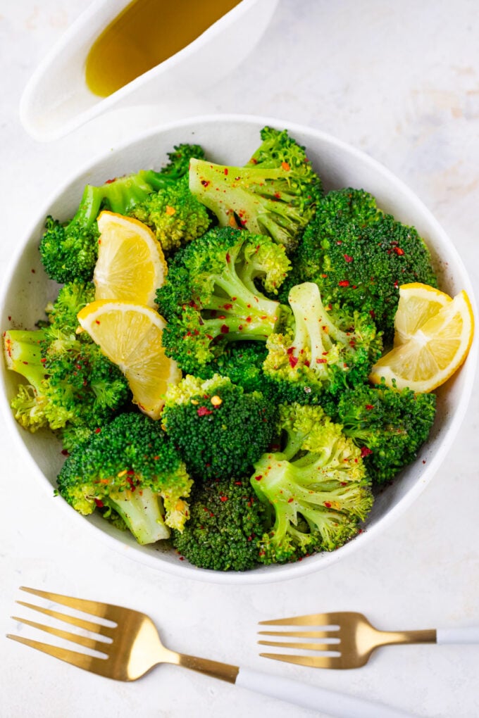 A bowl of steamed broccoli with lemon wedges.