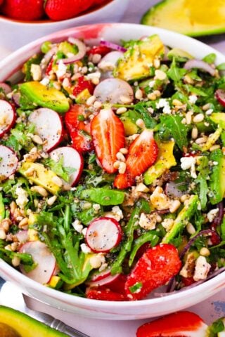 Overhead shot of a bowl of strawberry arugula salad with radishes, avocado, pine nuts.