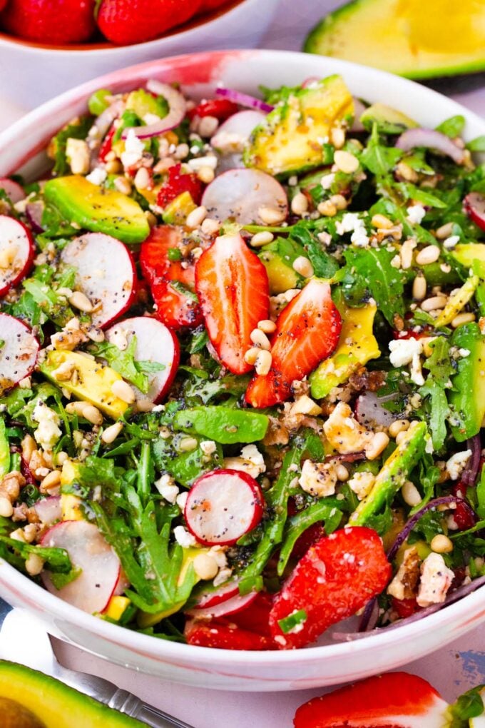 Overhead shot of a bowl of strawberry arugula salad with radishes, avocado, pine nuts.