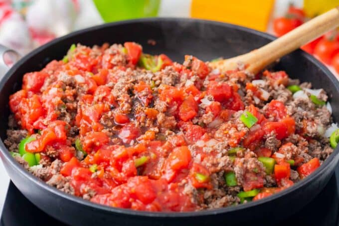 Stirring in diced tomatoes in a skillet with beef and veggies.