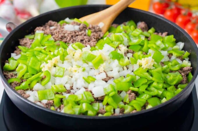 Adding diced greed bell pepper and onion to ground beef in a skillet.