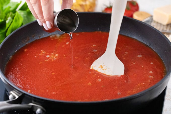 Adding vodka to tomato sauce to make penne alla vodka.