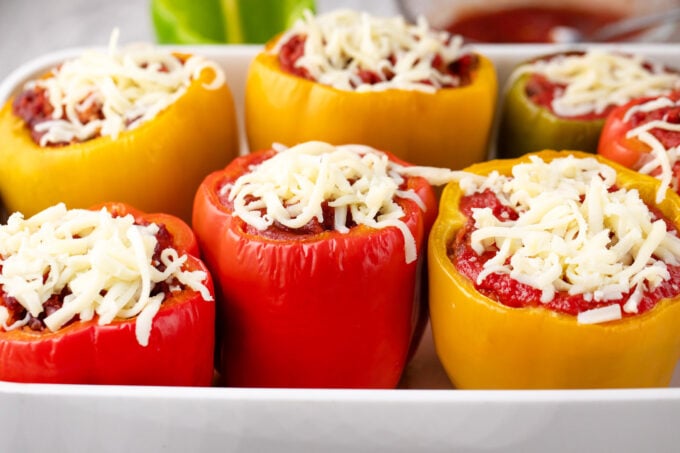 Topping stuffed peppers with shredded cheese.