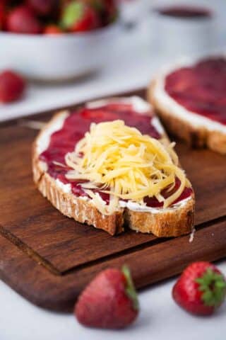 sourdough bread slice topped with cream cheese, strawberry jam, shredded cheddar