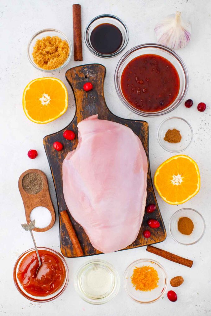 overhead shot of cranberry orange turkey breast ingredients arranged in bowls on a table around a turkey breast placed on a cutting board