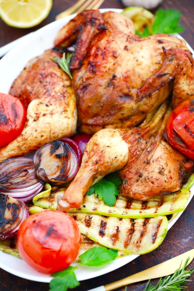 Golden brown grilled whole chicken on a platter with grilled veggies.