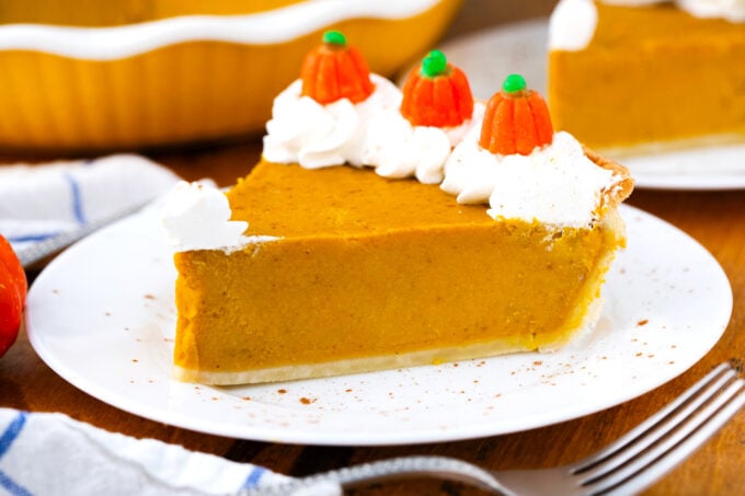 A slice of homemade pumpkin pie topped with whipped cream and candy pumpkins.