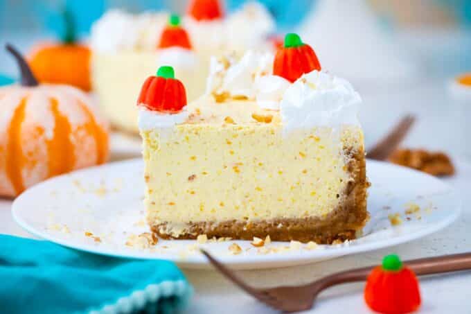 a slice of instant pot pumpkin cheesecake on a plate, garnished with whipped cream and candy pumpkins.