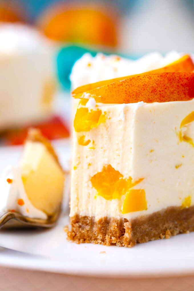 Close shot of a slice of no bake peach cheesecake with peach pieces.