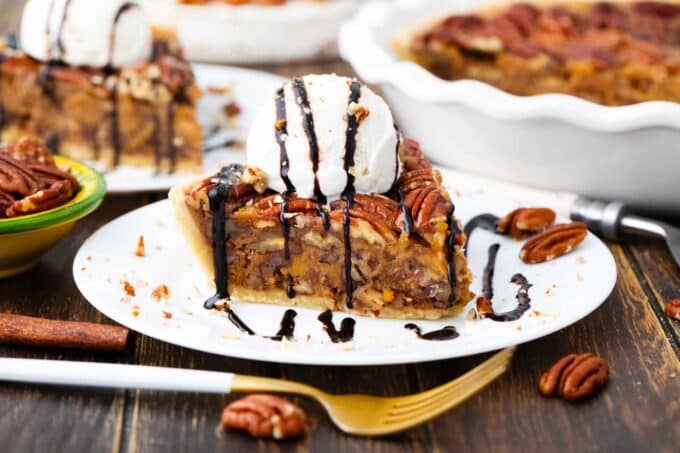 a slice of pecan pie topped with ice cream and chocolate sauce