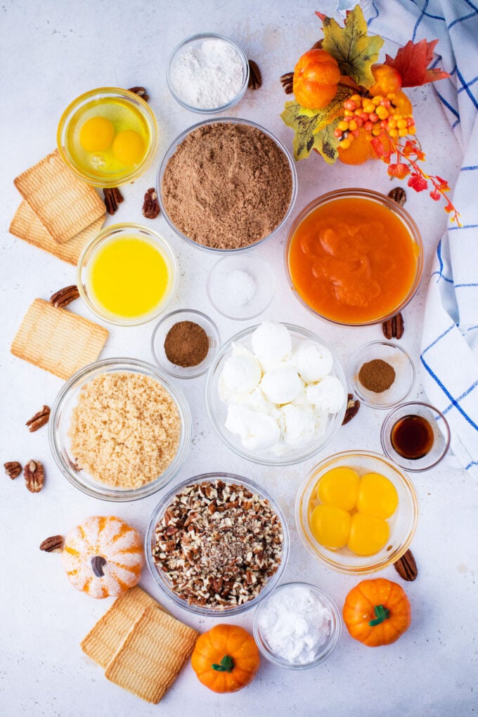 Pecan pie pumpkin cheesecake ingredients in bowls on a white surface.